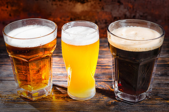 Three glasses with light, unfiltered and dark beer on wooden desk