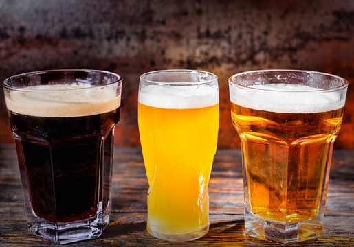 Three glasses with light, unfiltered and dark beer on dark wooden desk