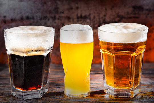 Three glasses with freshly poured light, unfiltered and dark beer on dark wooden desk