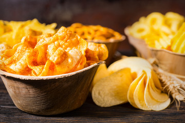 Close up of wooden plate with tasty corn chips near wooden plates with snacks on dark wooden desk