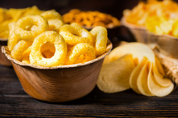 Close up of wooden plate with tasty corn snack near wooden plates with snacks on dark wooden desk