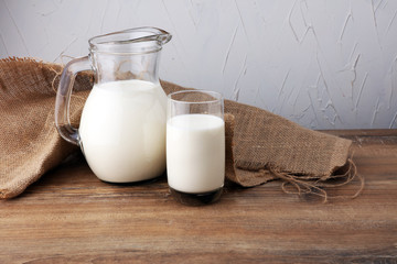 A jug of milk and glass of milk on a wooden table.