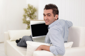 Handsome man is using a laptop, looking at camera and smiling