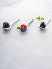 Fresh berries on spoons on gray background. One raspberry between two blackberries