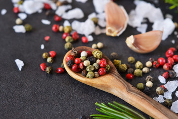 Mix of peppers with salt, rosemary and garlic on shale stone. Black food background with spices. Top view.