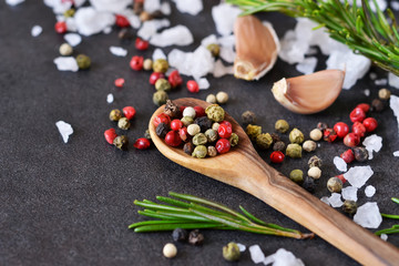 Mix of peppers with salt, rosemary and garlic on shale stone. Black food background with spices. Top view.