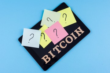 Word bitcoin in abstract letters and question questions on stickers glued to the tablet.