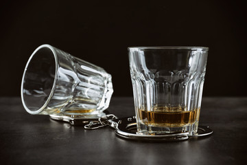 Glasses with handcuffs on dark background. Alcohol dependence concept