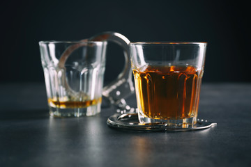 Glasses with handcuffs on dark background. Alcohol dependence concept