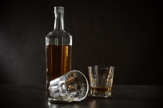 Bottle and glasses with handcuffs on dark background. Alcohol dependence concept