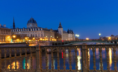 Conciergerie Building in Paris, France at night with lights reflection in the Seine River water.