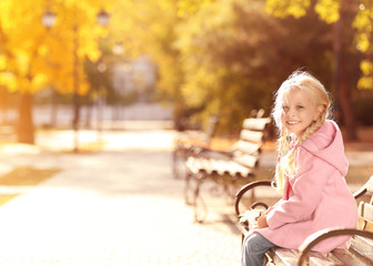 Cute little girl sitting on bench in autumn park