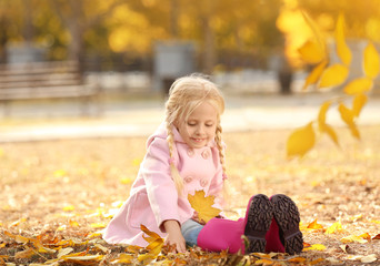 Cute little girl sitting on ground in autumn park