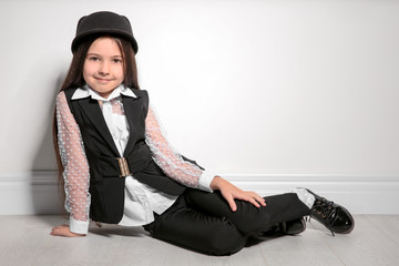 Adorable stylish girl sitting near light wall
