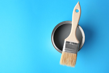 Tin can with grey paint and brush on color background, top view
