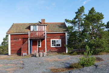 Red wooden abandoned cottage built on the rock, pine trees in the background