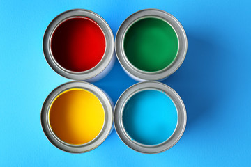 Multicolored paint in tin cans on color background, top view