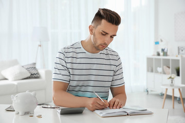 Young man counting taxes at table indoors