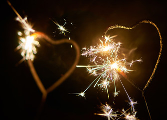 Two bengal lights in the shape of a heart burning bright on the dark background