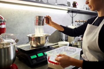 A woman sifts the flour through a sieve in the kitchen