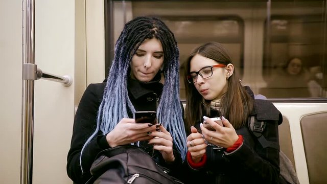 girl with dreadlocks is going by metro with her friend, teens are sitting and taking selfies by phones