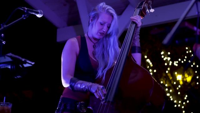Closeup of female stand-up or double bass player with pierces and tattoos under blue lights.