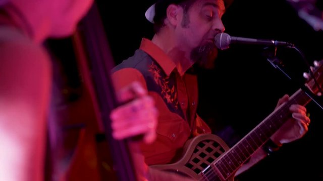 Closeup of roots musician playing a resonator and singing into a microphone.