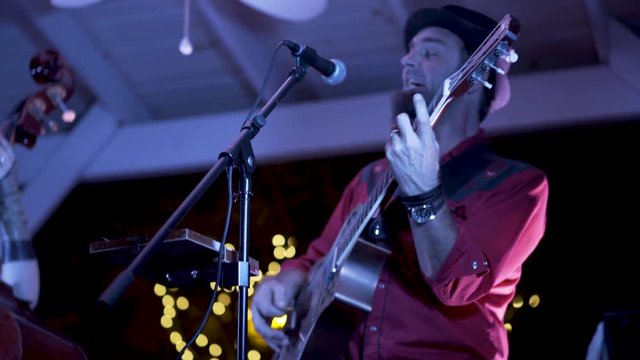 Closeup of guitarist playing resonator and singing at an outdoor concert at a restaurant at night.