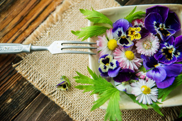 Fresh salad with smoked salmon, black olives, cherry tomatoes and edible flowers on wooden background.