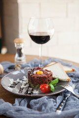 beautiful serving of beef tartare with quail egg yolk with two slices of bread and a glass of wine on a gray plate