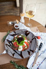 Italian classic caprese salad with pesto sauce on a gray ceramic plate with a glass of white wine