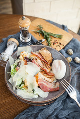 Caesar salad with bacon and poached egg on a wooden table