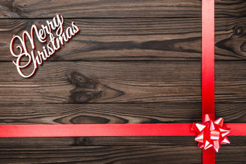 View from above of a Merry Christmas inscription on dark brown wooden background with red ribbon,...