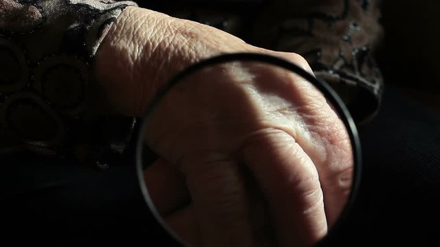 Looking through the magnifying glass on the wrinkled hands of the old lady
