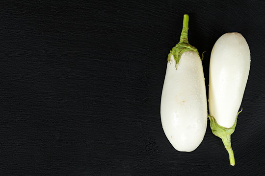 White eggplant on a black stone surface with water drops. Top view. Copy space.