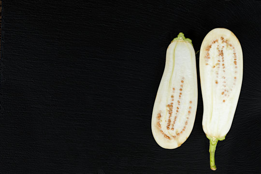 White hite eggplant on a black stone surface. The half eggplant. Top view. Copy space.