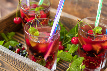 Glasses of refreshing  drink flavored with fresh fruit and decorated with cherries covered with dew drops. Wooden background