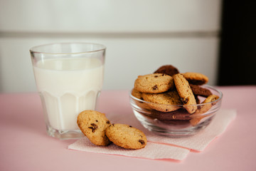 Glass of milk and chocolate chip cookies on the pink table, simple breakfast