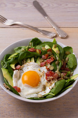 Egg with quinoa, avocado, bacon, spinach and pumpkin seeds in white bowl. Ideal dish for breakfast, vertical