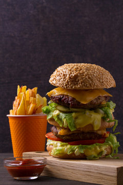 Homemade triple decker burger and fries on dark wooden background, vertical