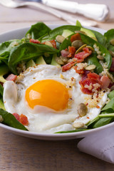 Egg with quinoa, avocado, bacon, spinach and pumpkin seeds in white bowl. Ideal dish for breakfast, vertical