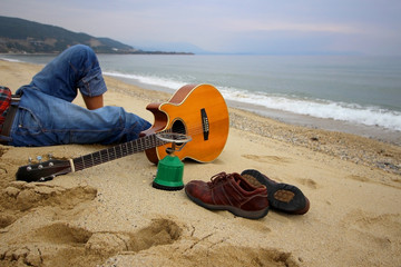 Man sitting on the beach with guitar and shoes. Travel conception.