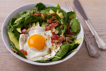 Egg with quinoa, avocado, bacon, spinach and pumpkin seeds in white bowl. Ideal dish for breakfast, horizontal
