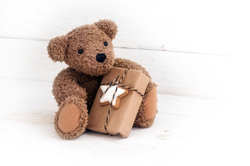 Teddy bear with a Christmas present sitting on a white painted wooden background, copy space