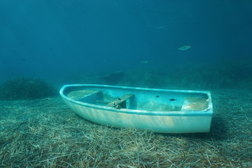 Underwater a small boat sunken on the seabed with leaves of Neptune grass and some fish, Mediterranean sea, Catalonia, Costa Brava, Spain