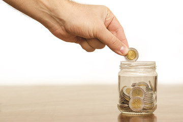 Hand Putting Coin in a Jar Full of Coins, Egyptian Pounds, Saving Concept, Isolated on White Background, Space for Text