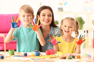 Young mother and cute kids with paint on face and hands indoors