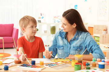 Cute boy with mother painting at table in room