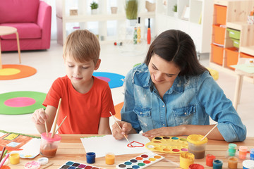 Cute boy with mother painting at table in room