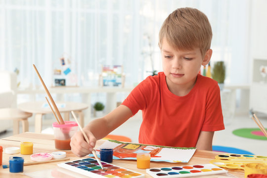 Talented boy painting at table in room
